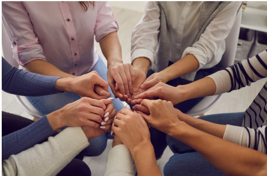 a group of people are sitting in a circle putting their hands together .