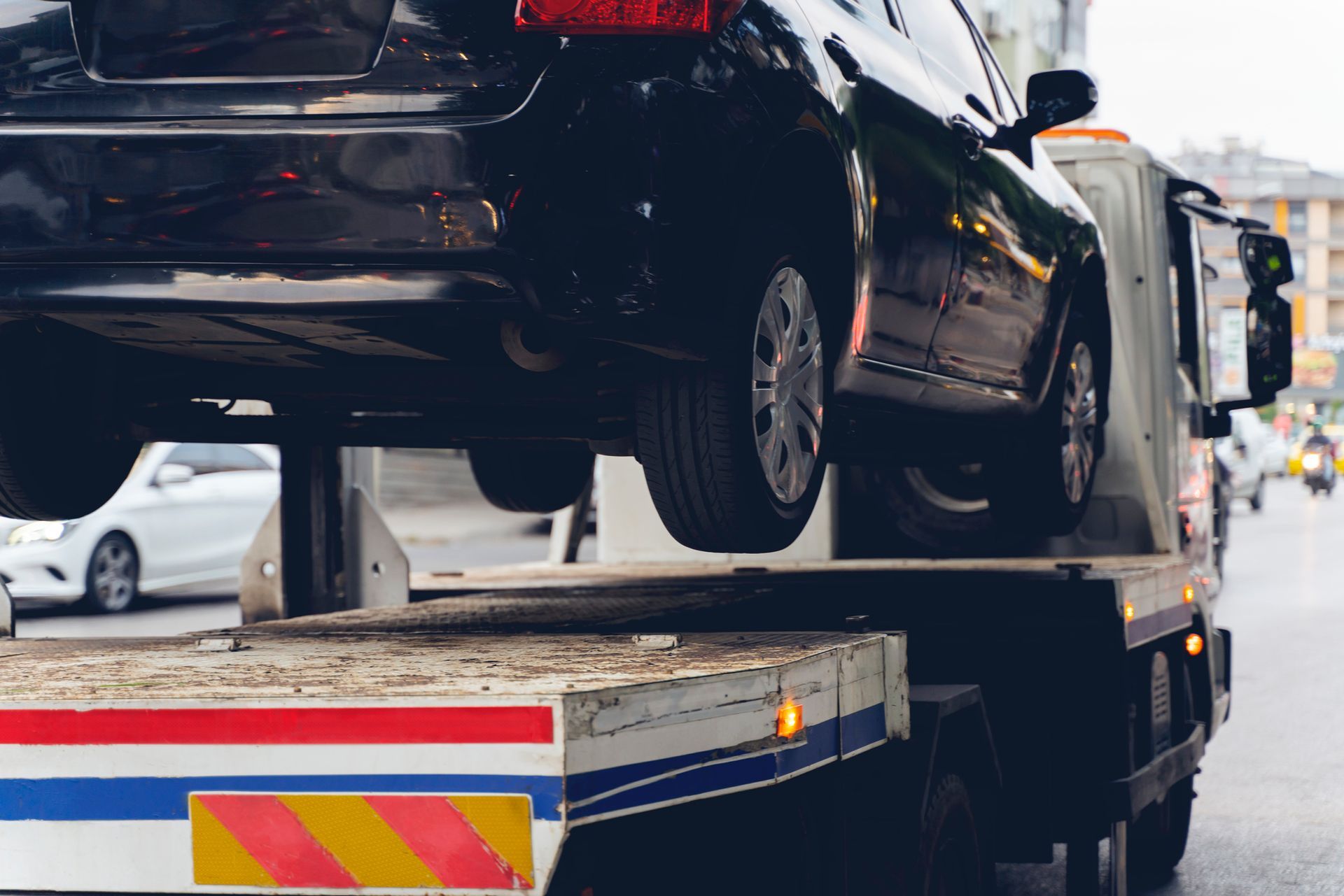 Black car being towed by a tow truck on a city street.
