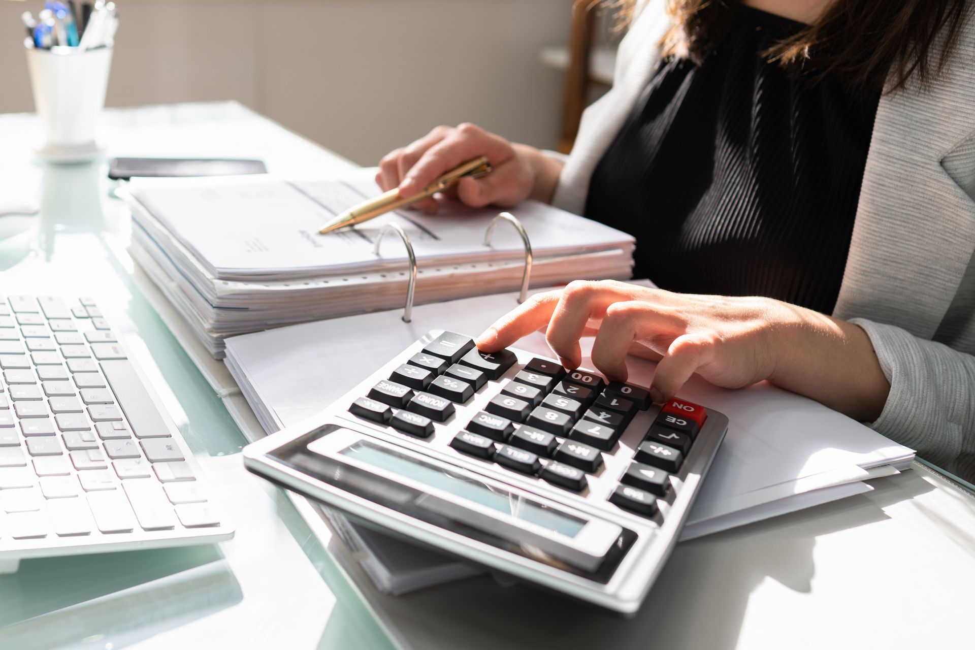 Woman using calculator, reviewing documents at a desk.