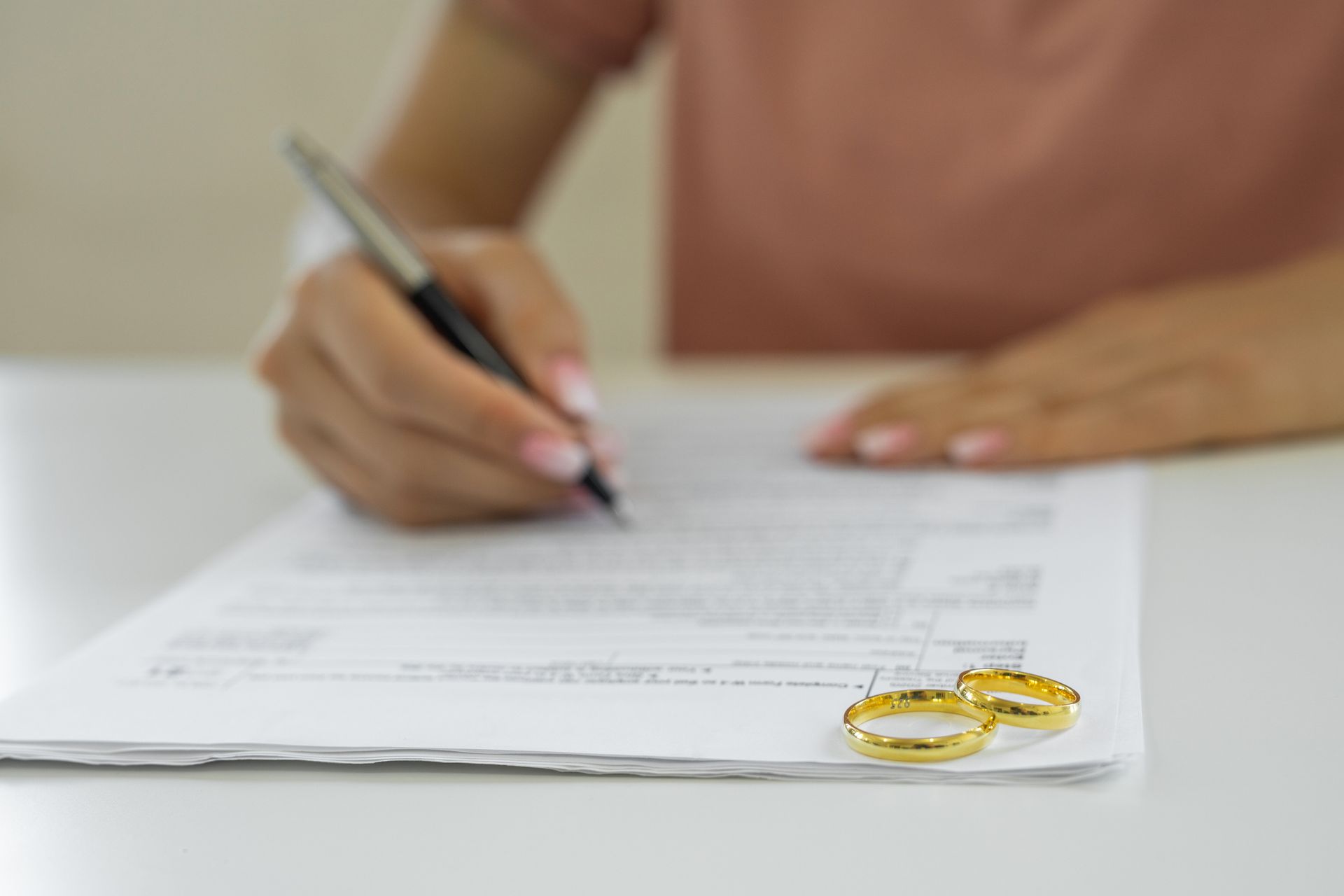 Person signing divorce papers with wedding rings in the foreground.