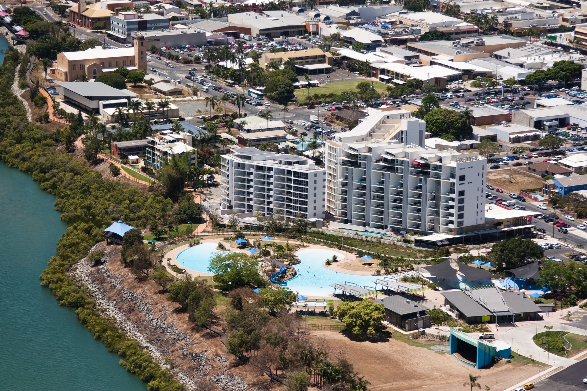 Aerial view of a coastal city with waterfront buildings, a lagoon pool, and surrounding greenery.