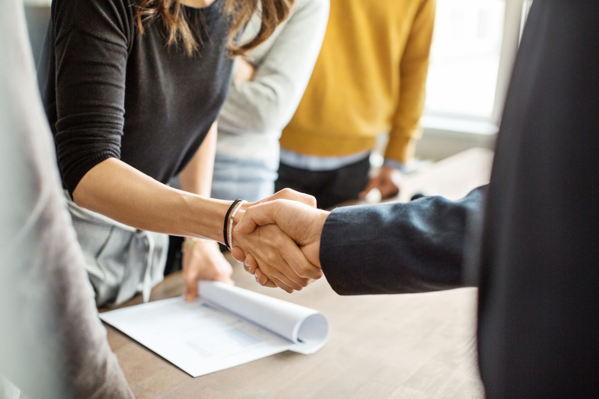 People shaking hands over a table, with a document, possibly an agreement.