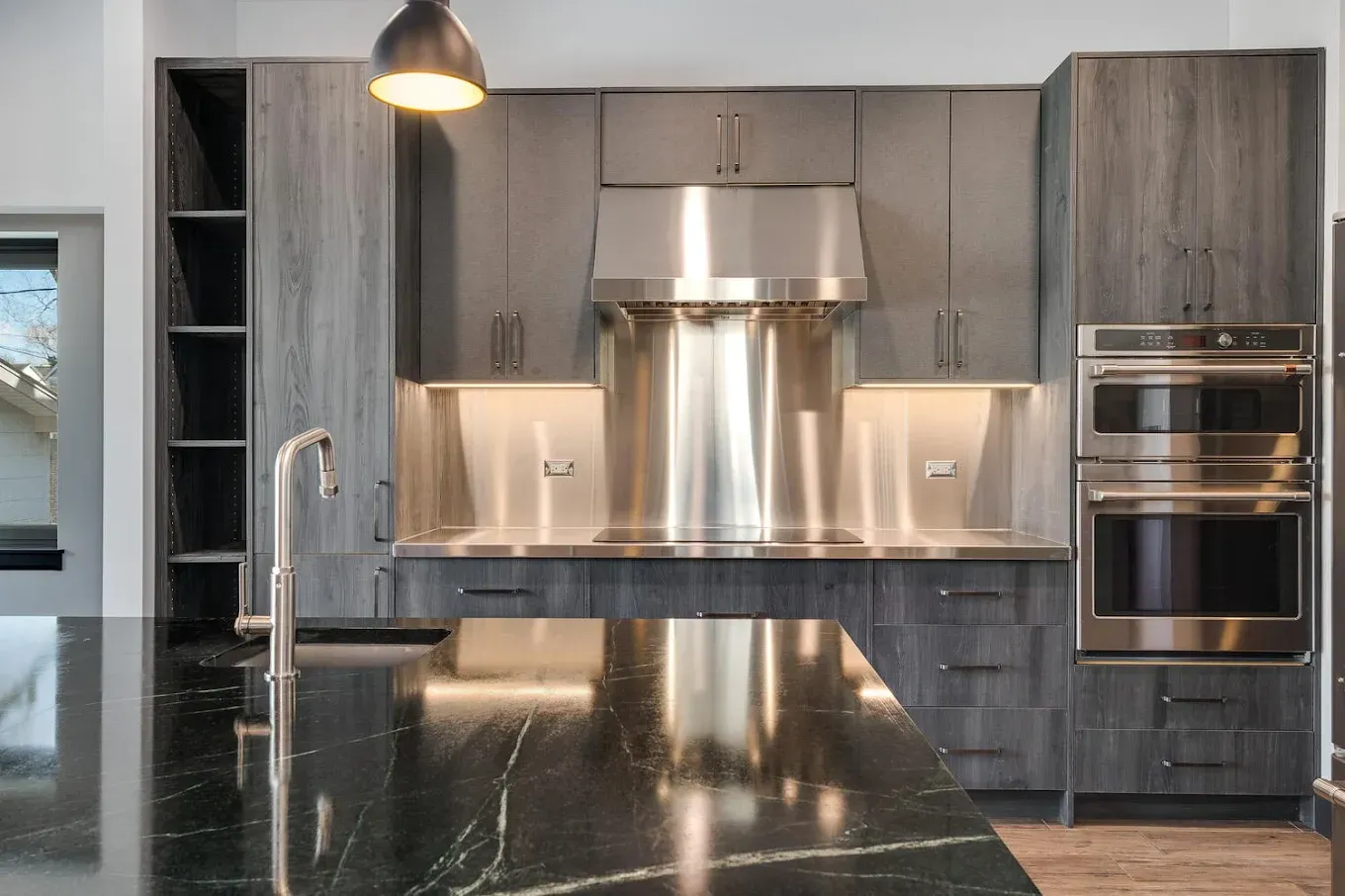 Modern kitchen with dark gray cabinets, stainless steel hood, and a black countertop island.
