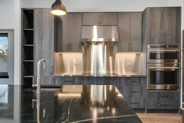 Modern kitchen with dark gray cabinets, stainless steel hood, and a black countertop island.