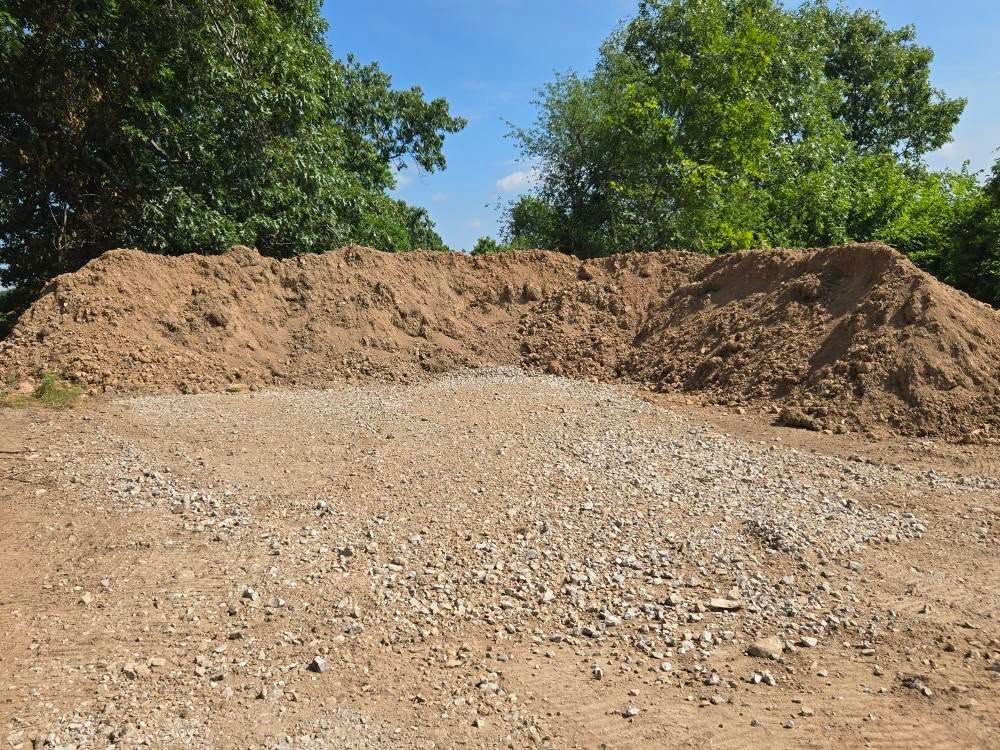 Pile of dirt and gravel with trees in background.