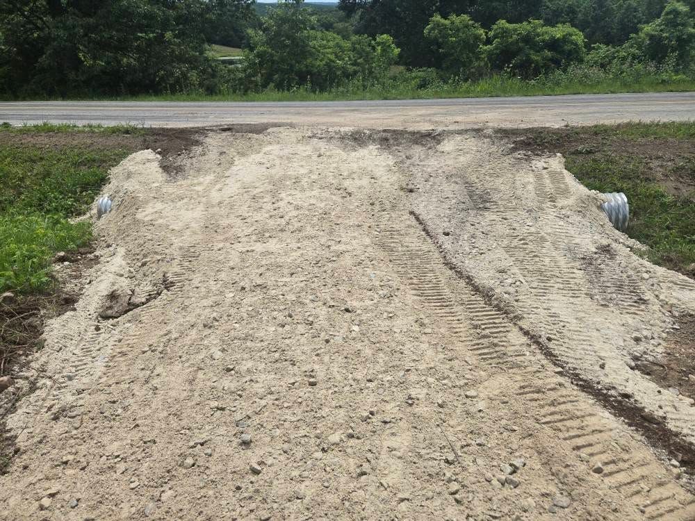 Dirt pile ramp across a road, likely for vehicles, with tire tracks.