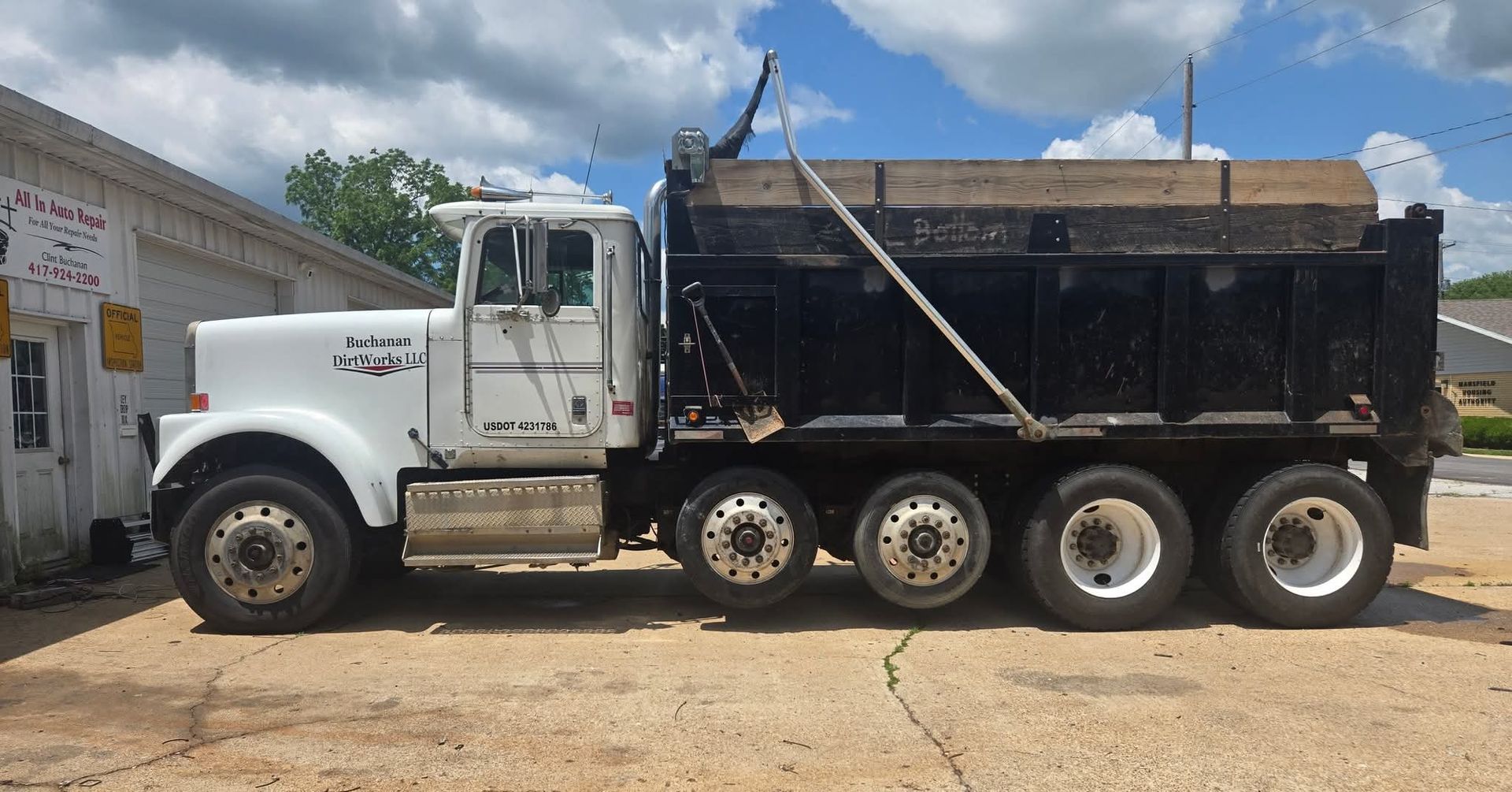 White and black dump truck parked on a gravel surface, next to a white building, under a blue sky.