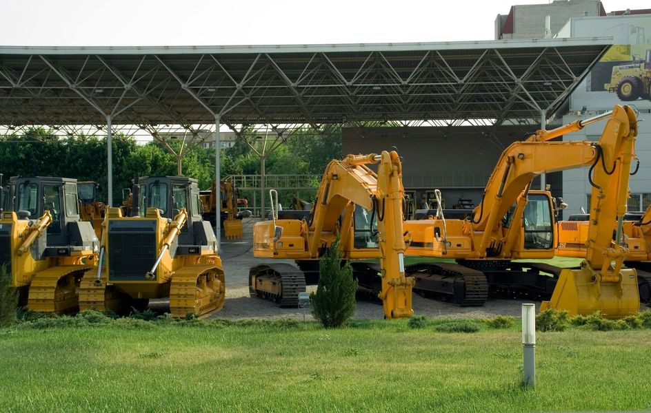 Yellow construction equipment parked under a shelter. Includes bulldozers and excavators in a grassy area.