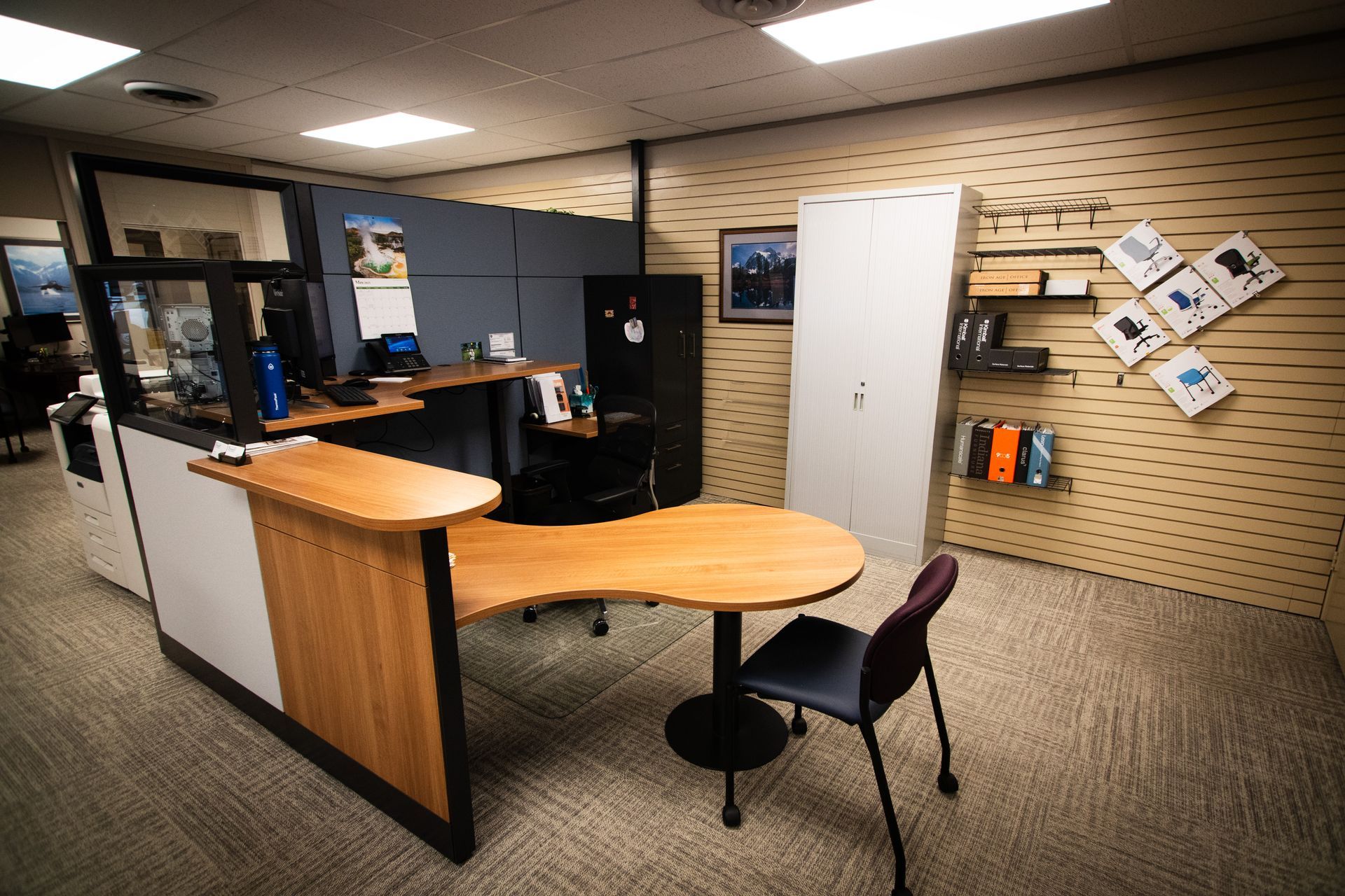 A cubicle in an office with a desk and a chair.