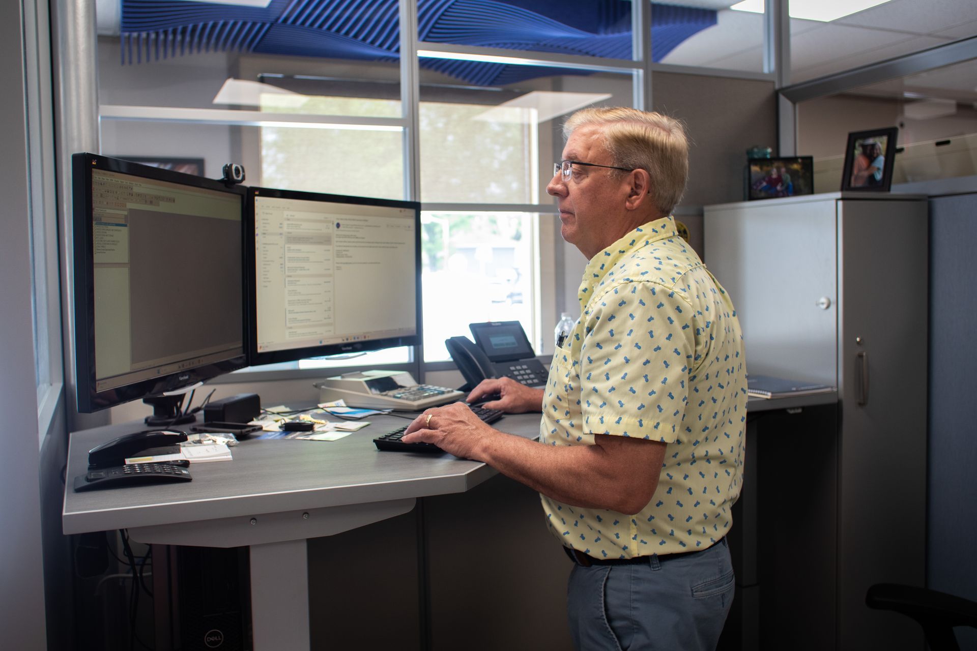 A man is standing at a standing desk in front of two computer monitors.
