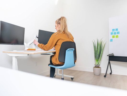 A woman is sitting at a desk in front of two computer monitors.