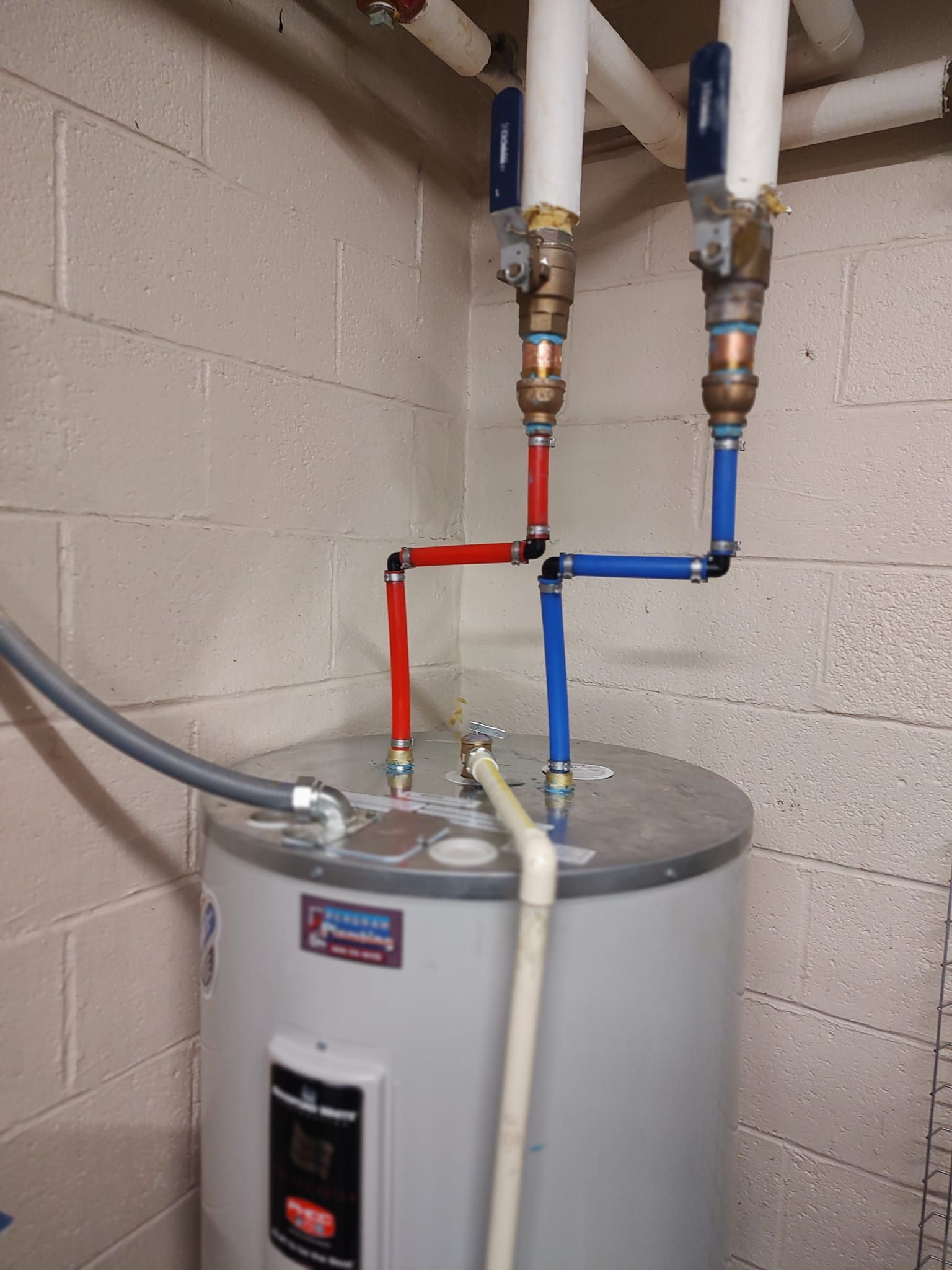 Water heater with red and blue pipes connected. White insulated pipes run overhead.