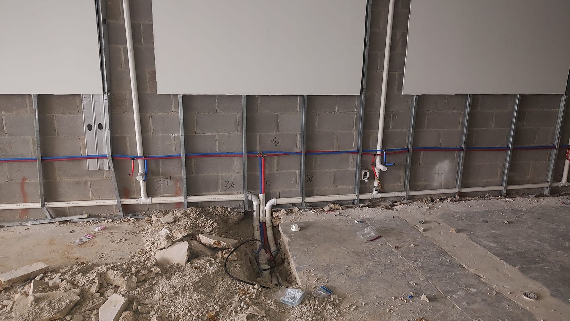Construction site interior: exposed plumbing and electrical lines in a partially demolished wall.