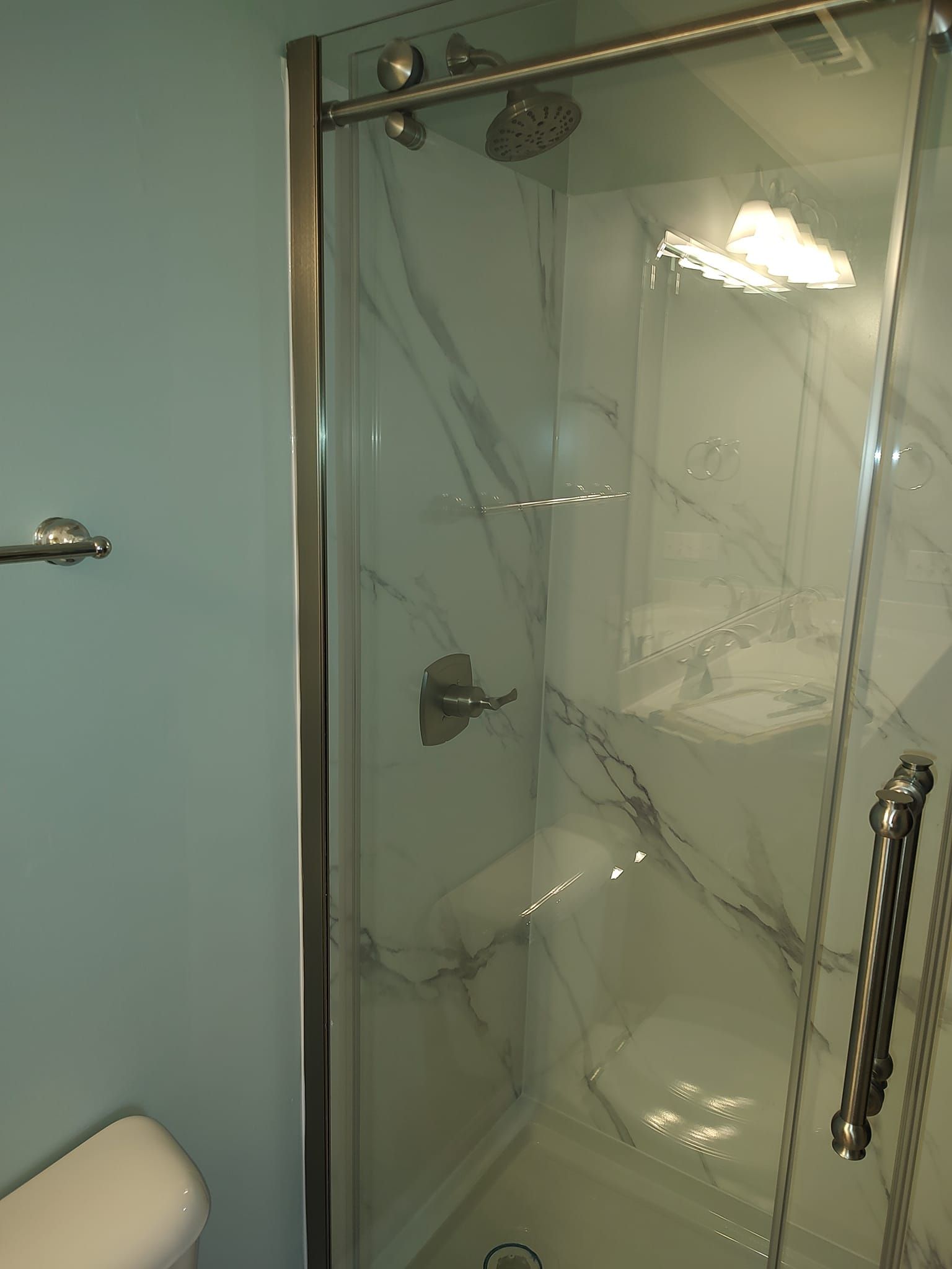 A walk-in shower with a glass door, silver fixtures, and marble-look tiles.
