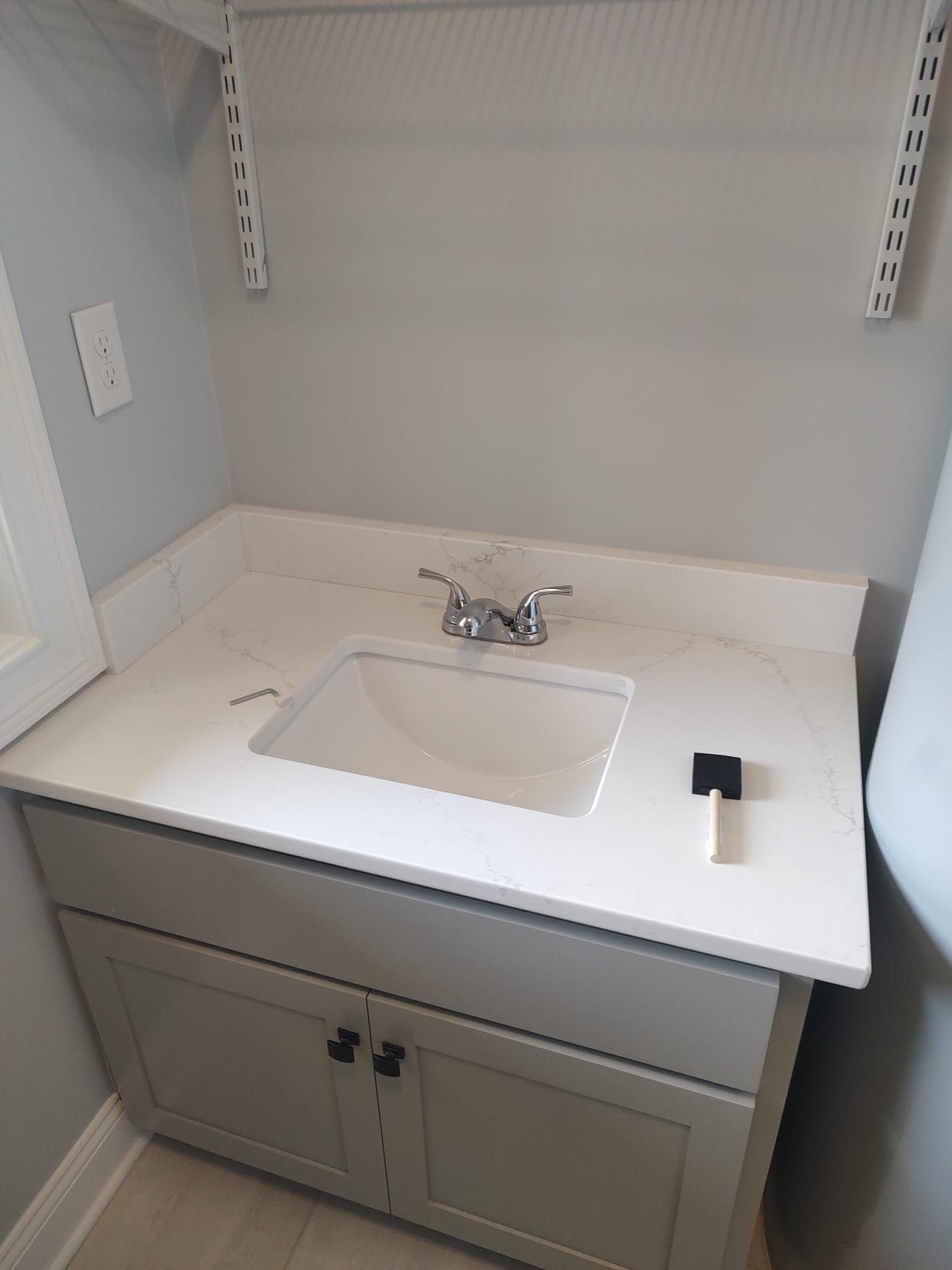 Gray bathroom vanity with white countertop and sink; gray cabinets below.