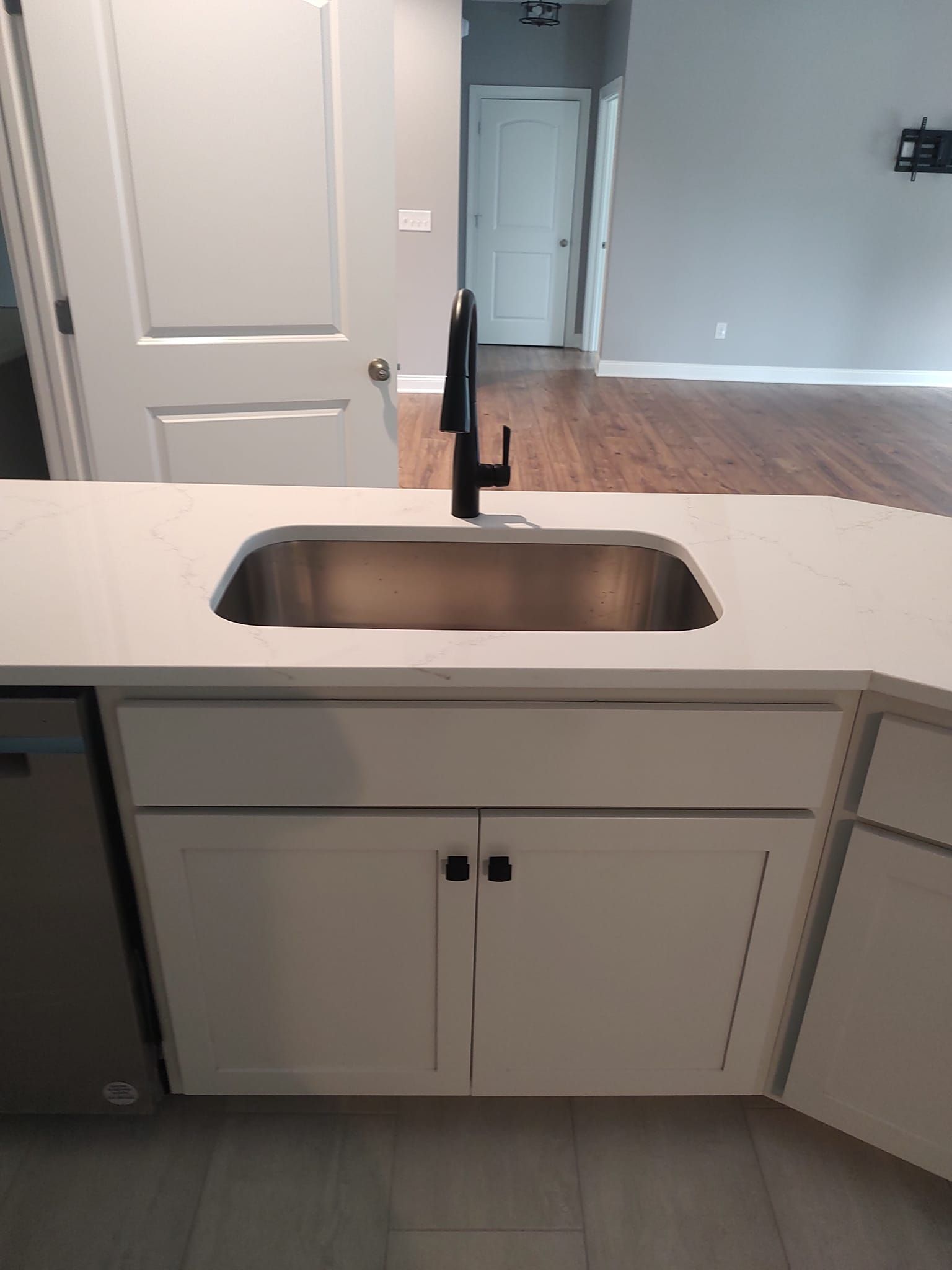 Kitchen island with stainless steel sink, black faucet, white cabinets, and white countertop.