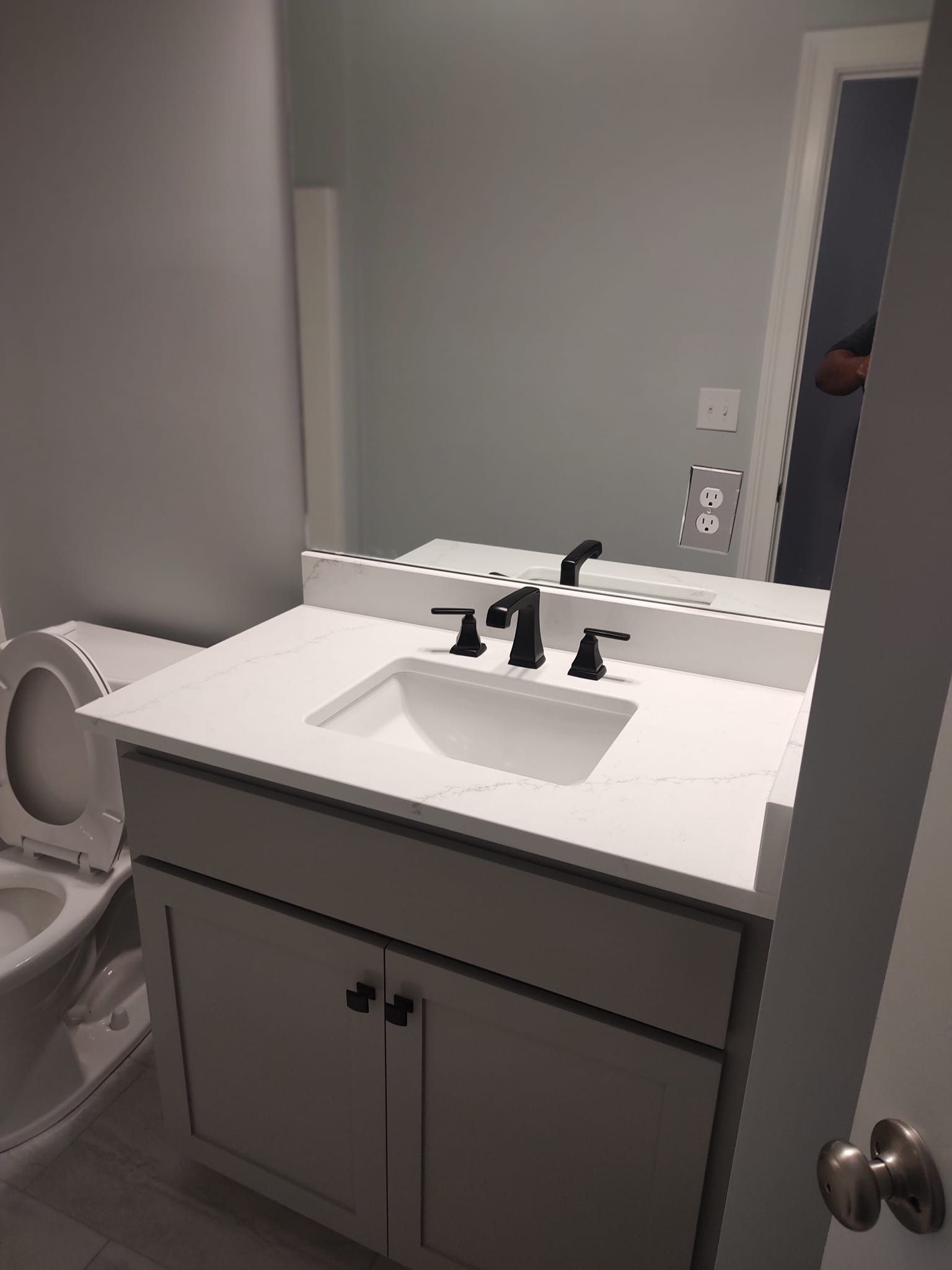Bathroom with white vanity, sink, black faucet, mirror, and toilet.