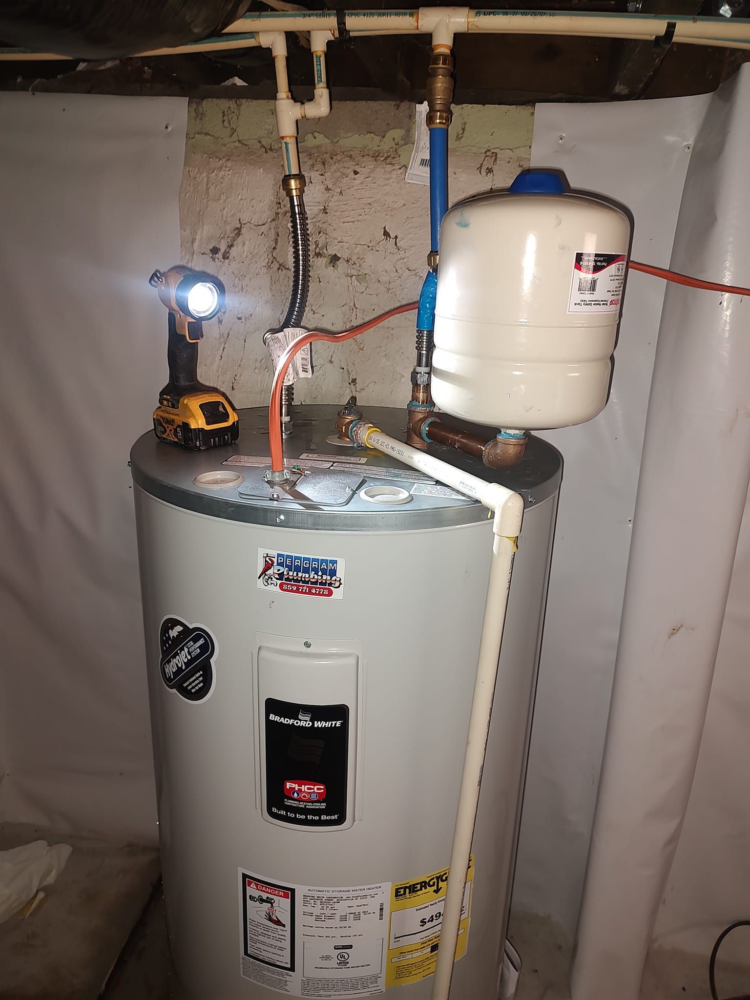 A water heater with connected pipes and a small expansion tank. A cordless drill rests on top.
