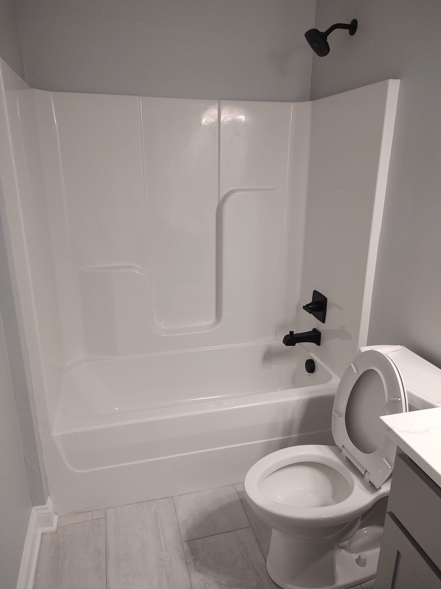 A white bathroom with a tub, toilet, black fixtures, and gray walls.