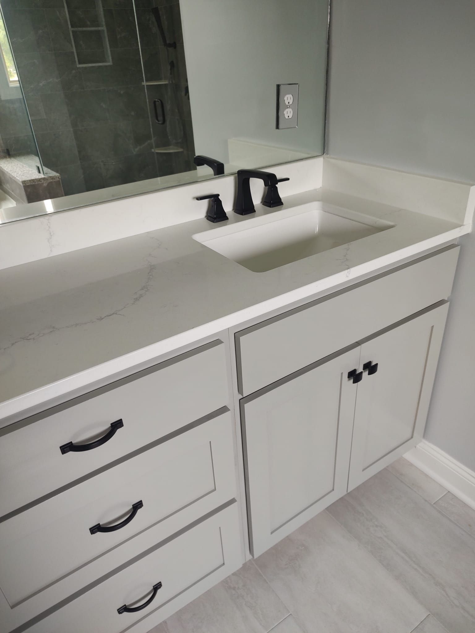 Bathroom vanity with gray cabinets, white countertop, and black faucet.