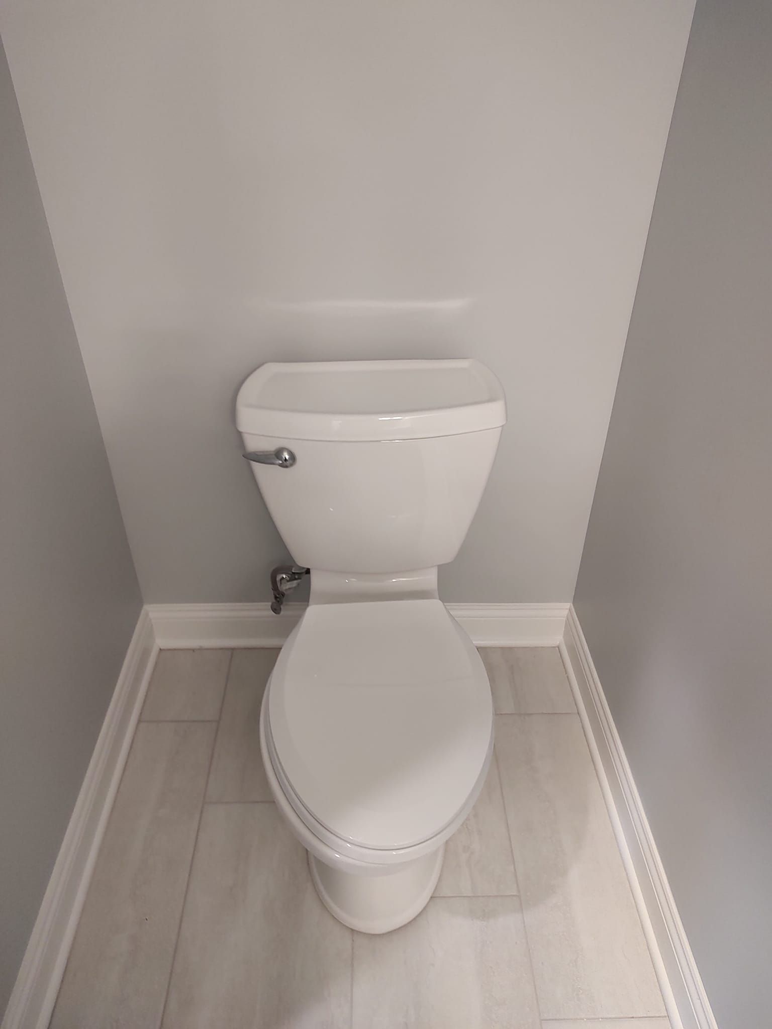 White toilet in a small bathroom with gray walls and light wood-look floor.