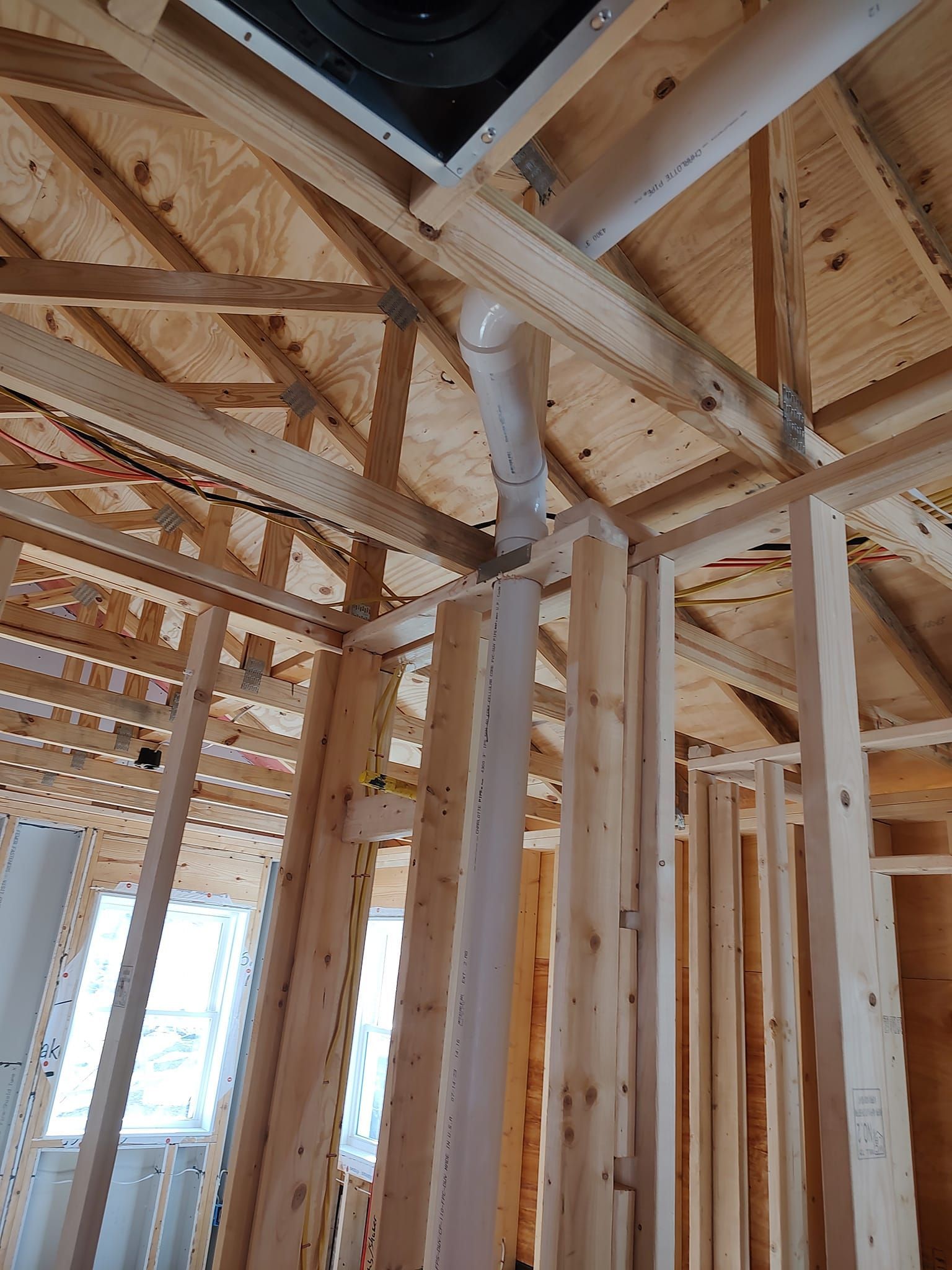 Interior view of a building under construction. Framing and plumbing pipes are visible in the wooden structure.