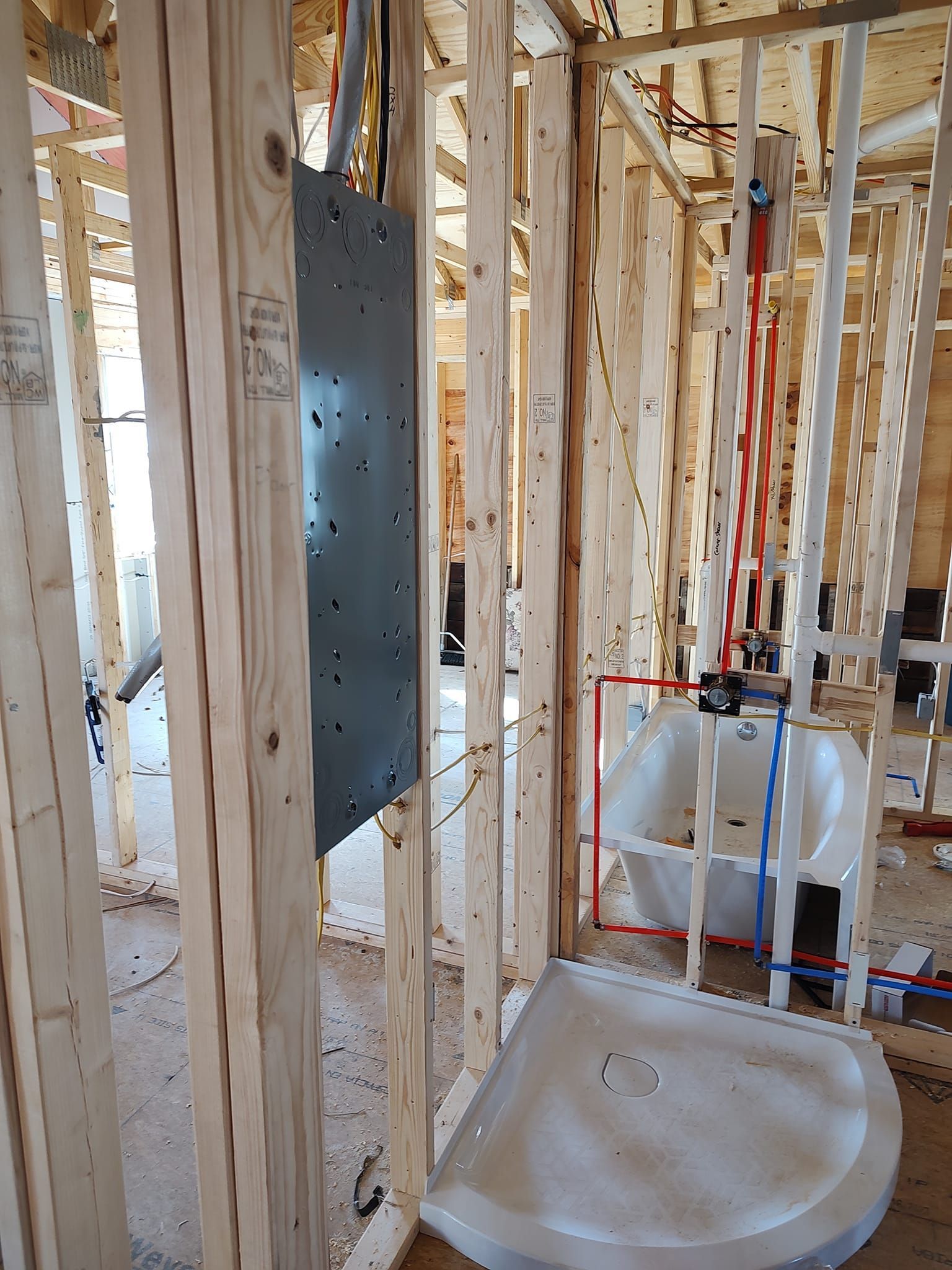 Interior view of a bathroom under construction; framing, bathtub, shower base, and plumbing visible.