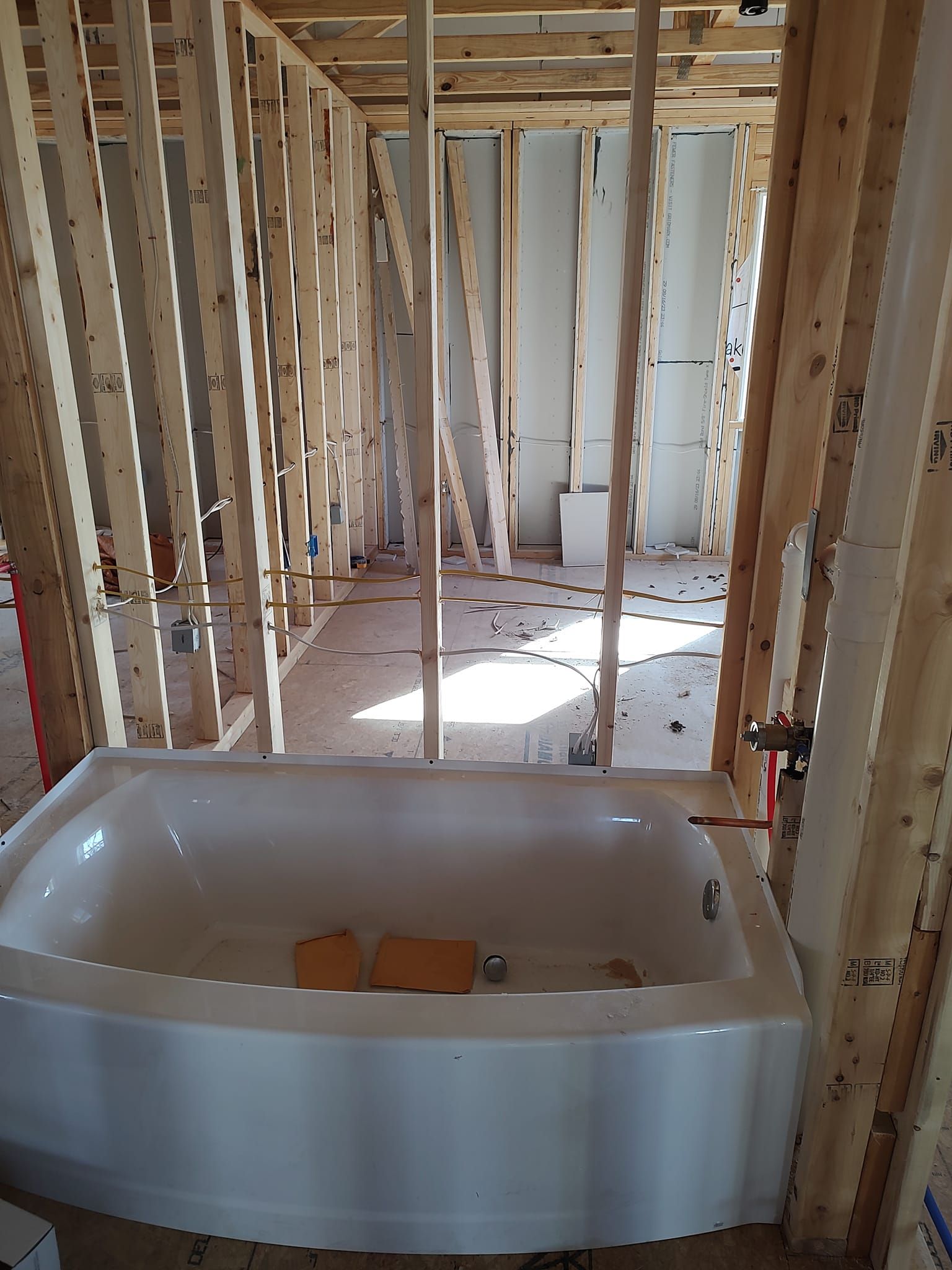 Bathtub framed in wooden studs, under construction. Bright room with concrete floor.