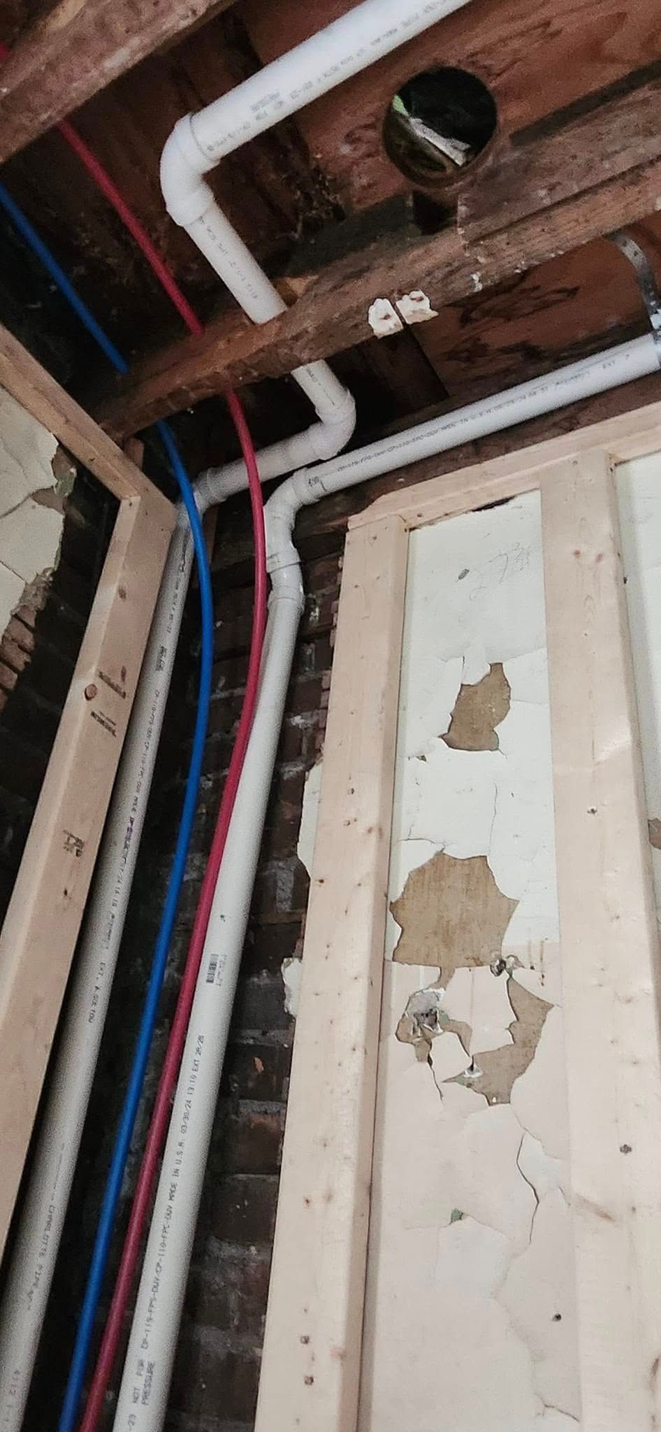 Pipes running through a wall and ceiling. White, blue, and red pipes. Wooden beams and walls.