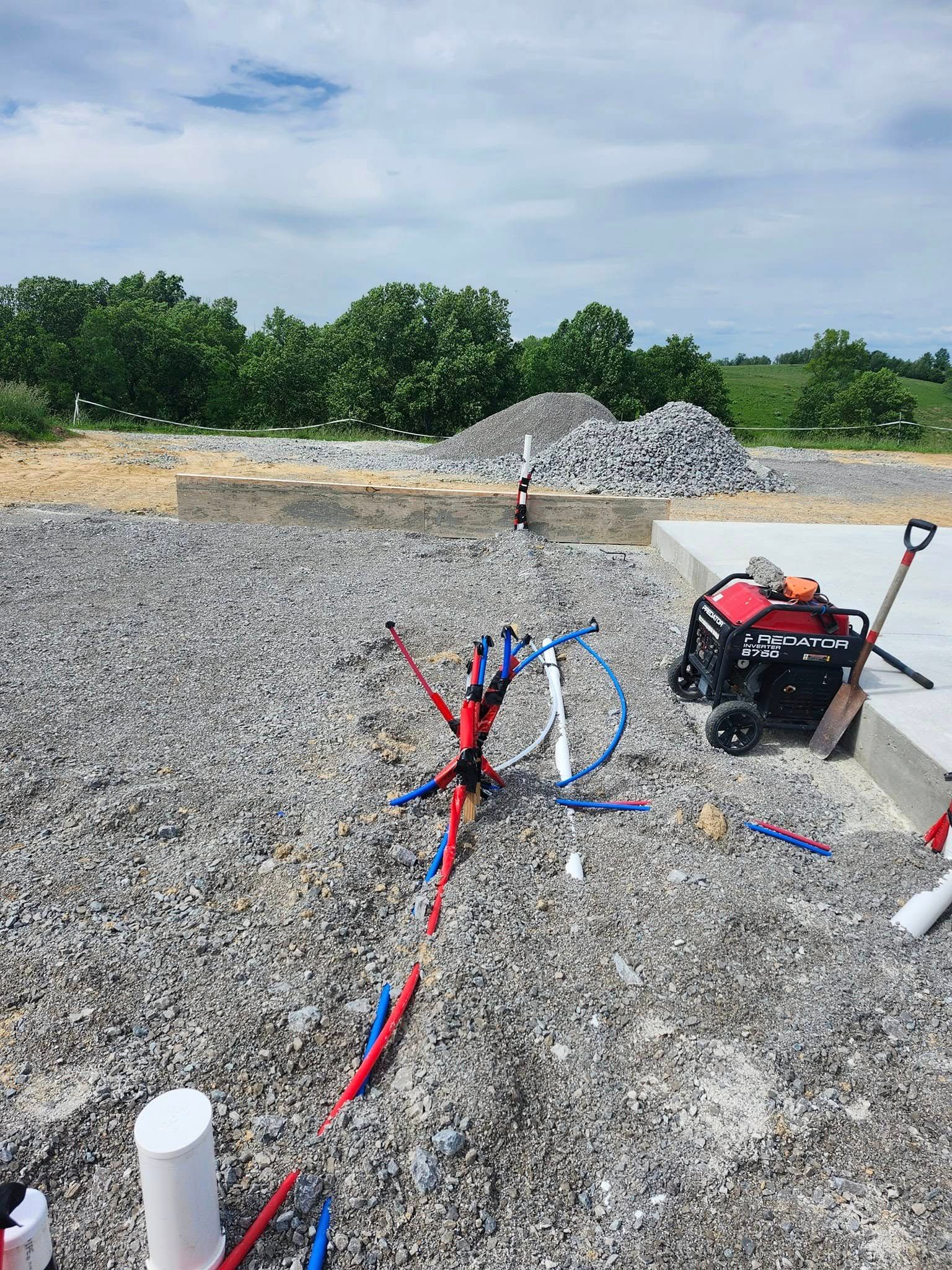 Pipes, gravel, and concrete foundation. Red and blue water lines. A generator and shovel sit nearby.