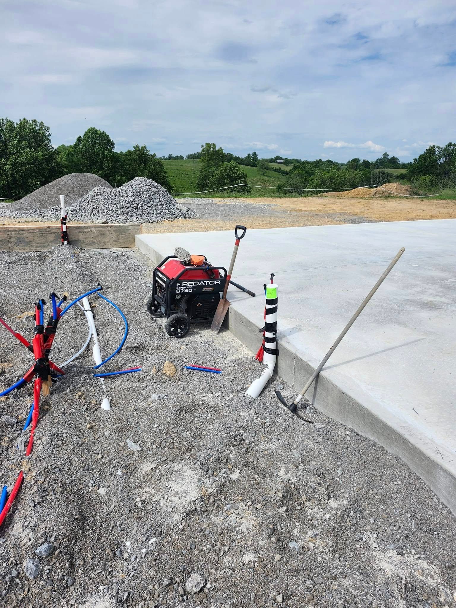 Construction site with gravel, concrete slab, generator, and plumbing.
