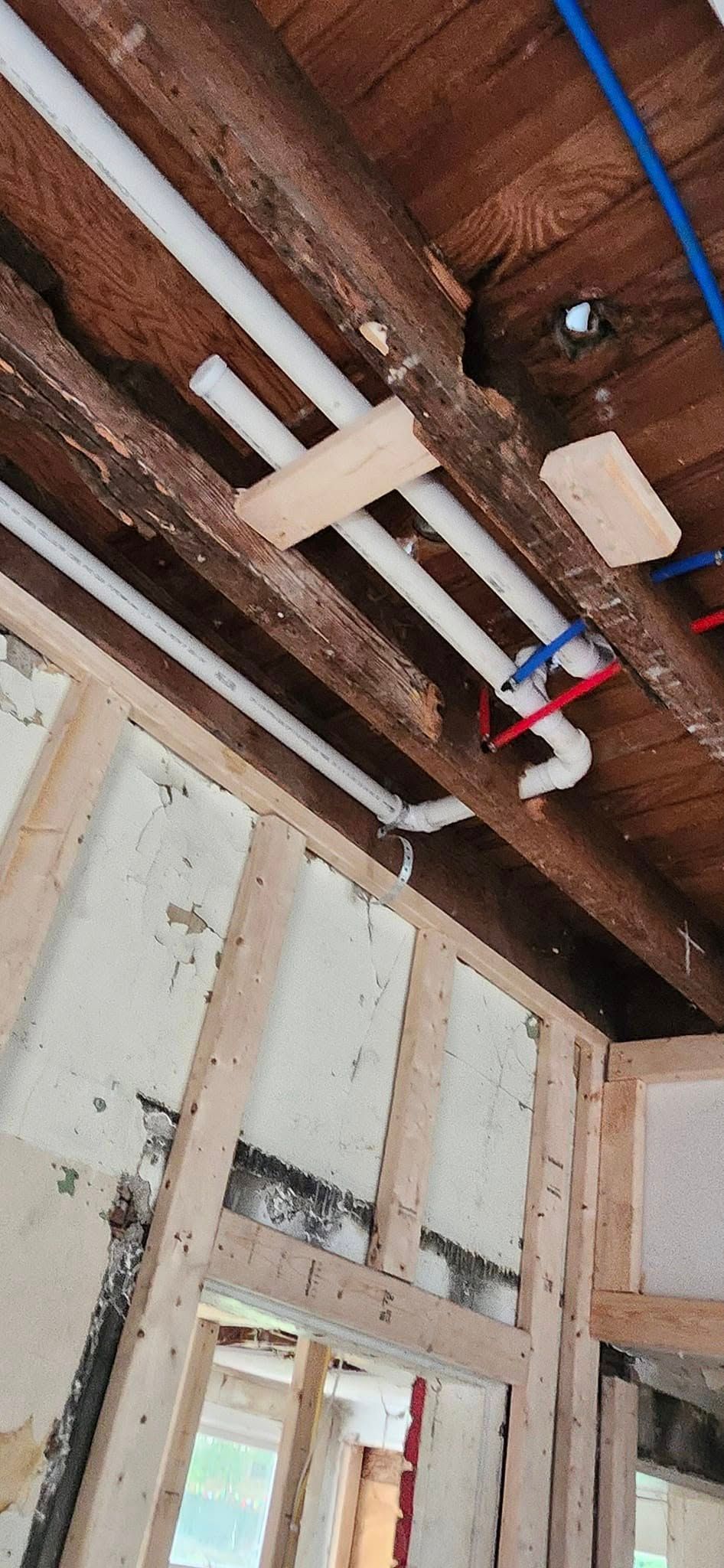 Interior view of exposed framing with pipes running along the ceiling. White insulation fills the wall cavities.