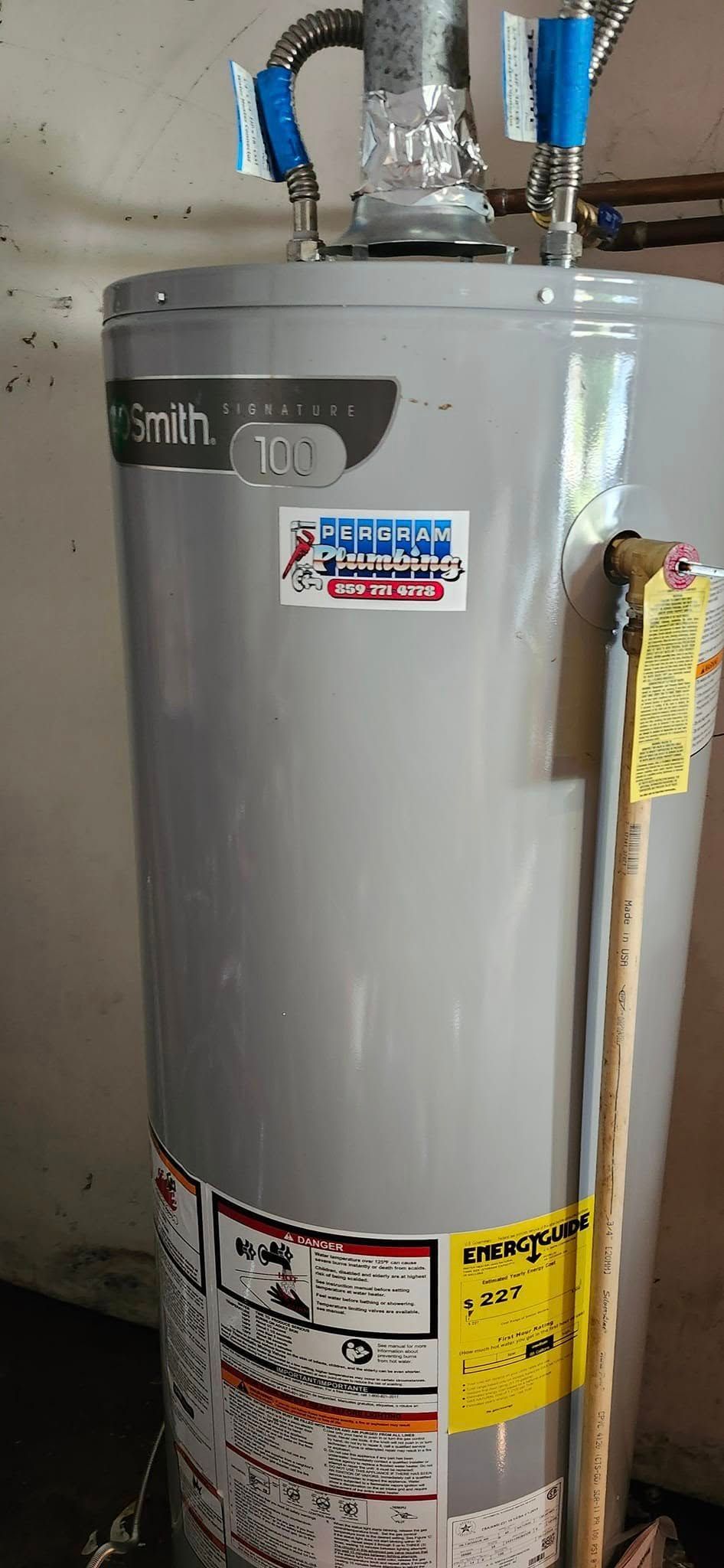 A tall, gray water heater with blue pipes and yellow stickers in a basement setting.