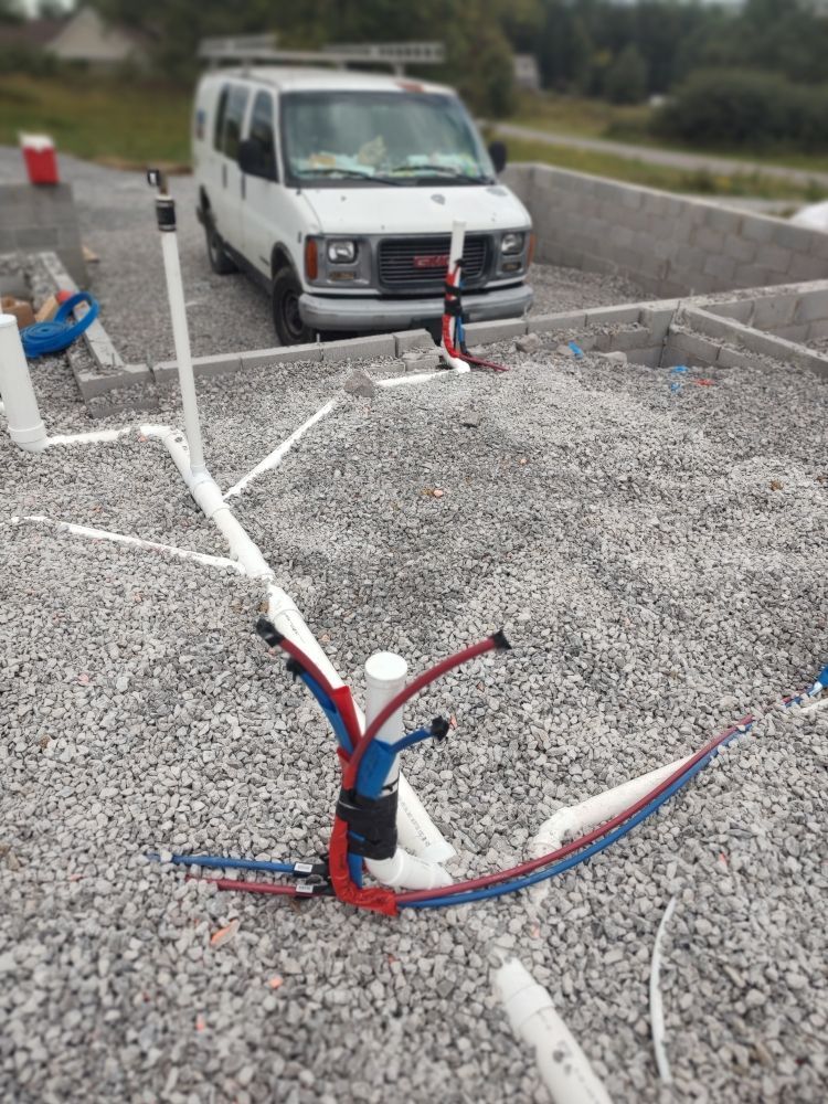 Plumbing pipes on gravel foundation with a white work van in the background.