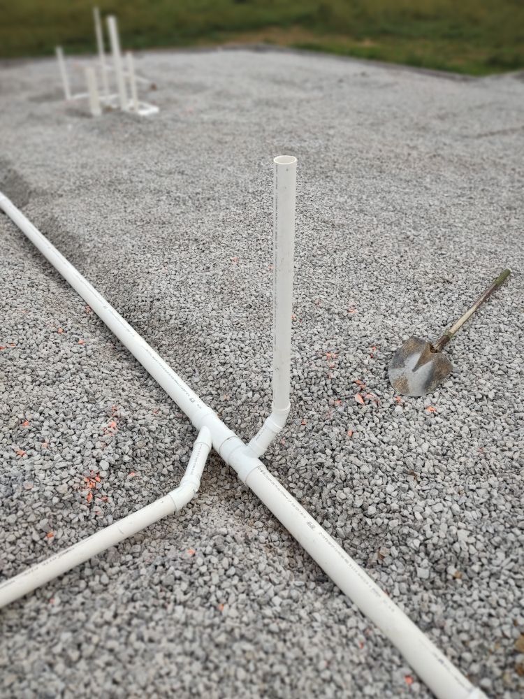 PVC pipes assembled on gravel ground. A shovel rests nearby.