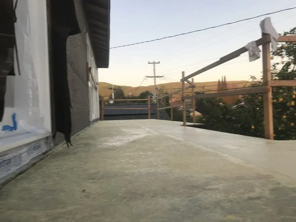 Flat rooftop with safety railings, view of distant hills and power lines under a light sky.