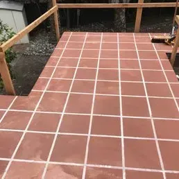 Red tiled outdoor patio with white grout, surrounded by wooden railing.