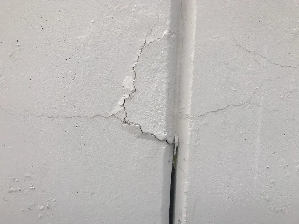 White wall with cracks around a vertical pipe.
