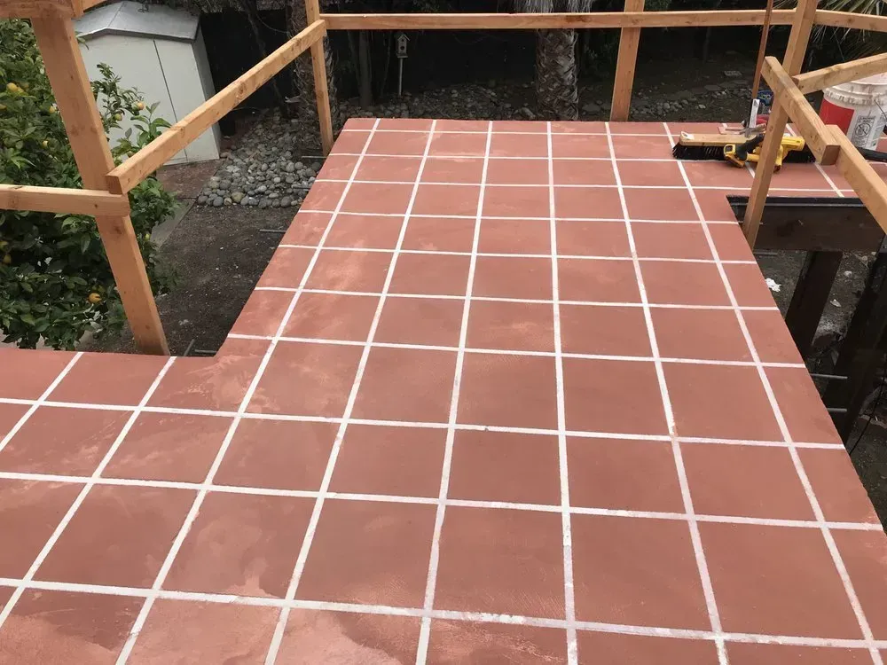 Red tiled deck with white grout, wooden railing, and a shed in the background.