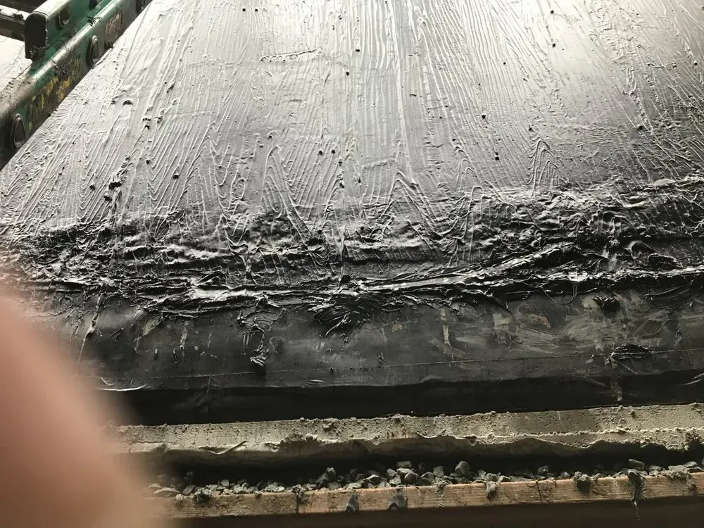 Black surface with thick, uneven, grayish-brown material layered on top, likely a sealant or adhesive.