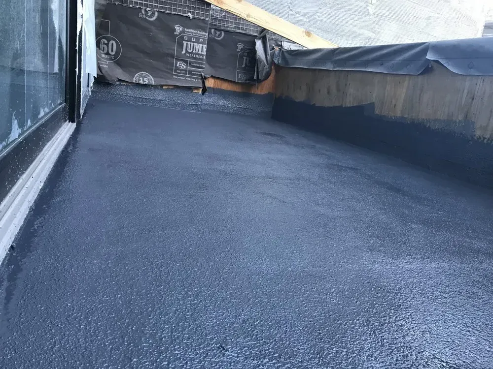 Black waterproof coating on a rooftop terrace. Dark gray surface with a wooden border.