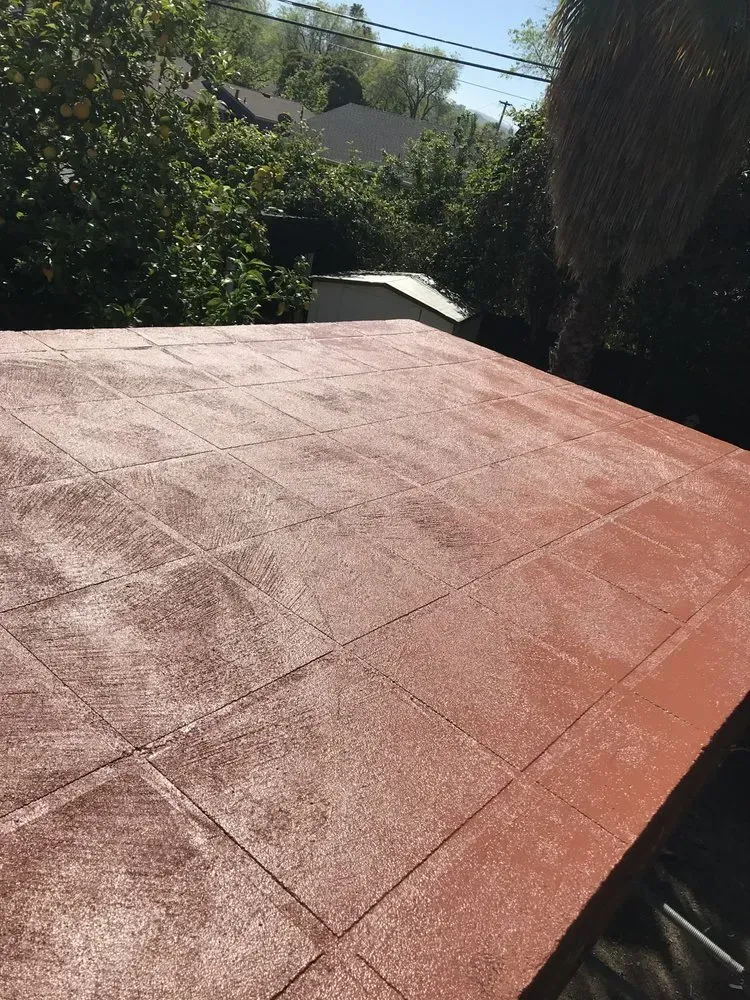 Red tile patio on a rooftop, surrounded by trees, with a sunny sky in the background.