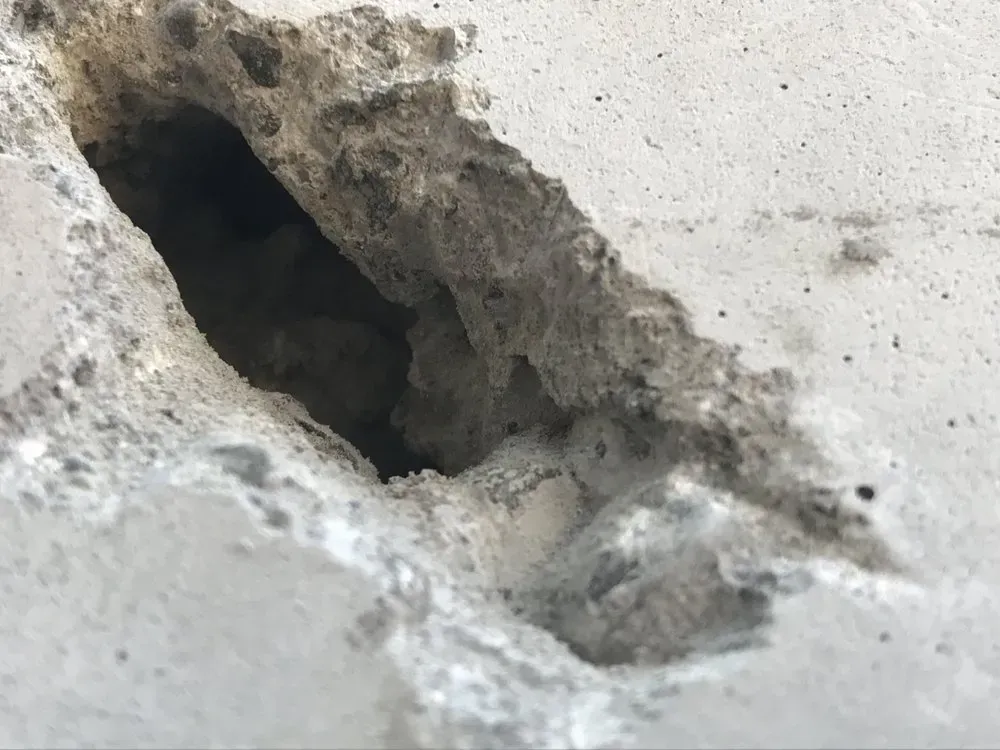 Close-up of a hole in a concrete wall, exposing the interior and showing the rough, gray texture.