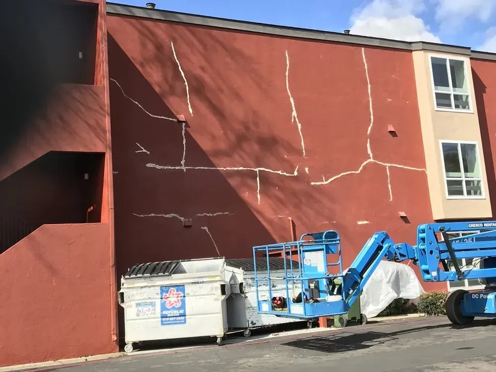 Red building with large cracks, a dumpster, and a blue lift.