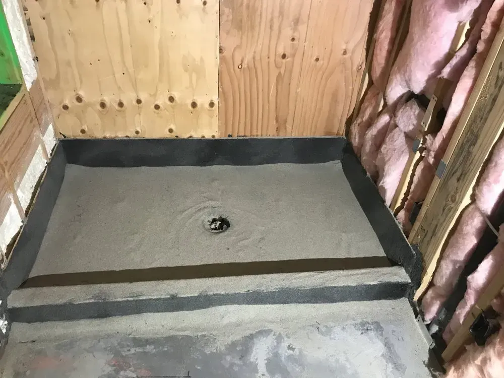 Shower base with cement floor, drain, and waterproof lining; wood and insulation visible.