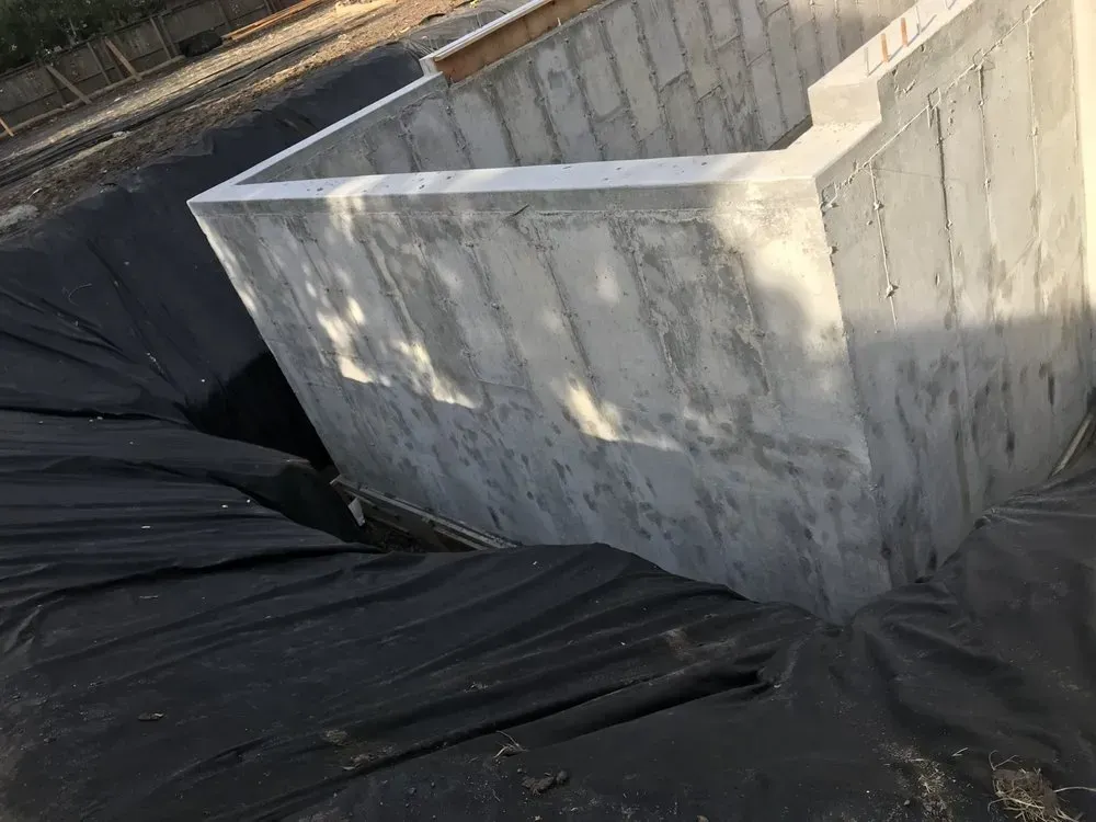 A concrete foundation wall with a dark liner in a construction site.