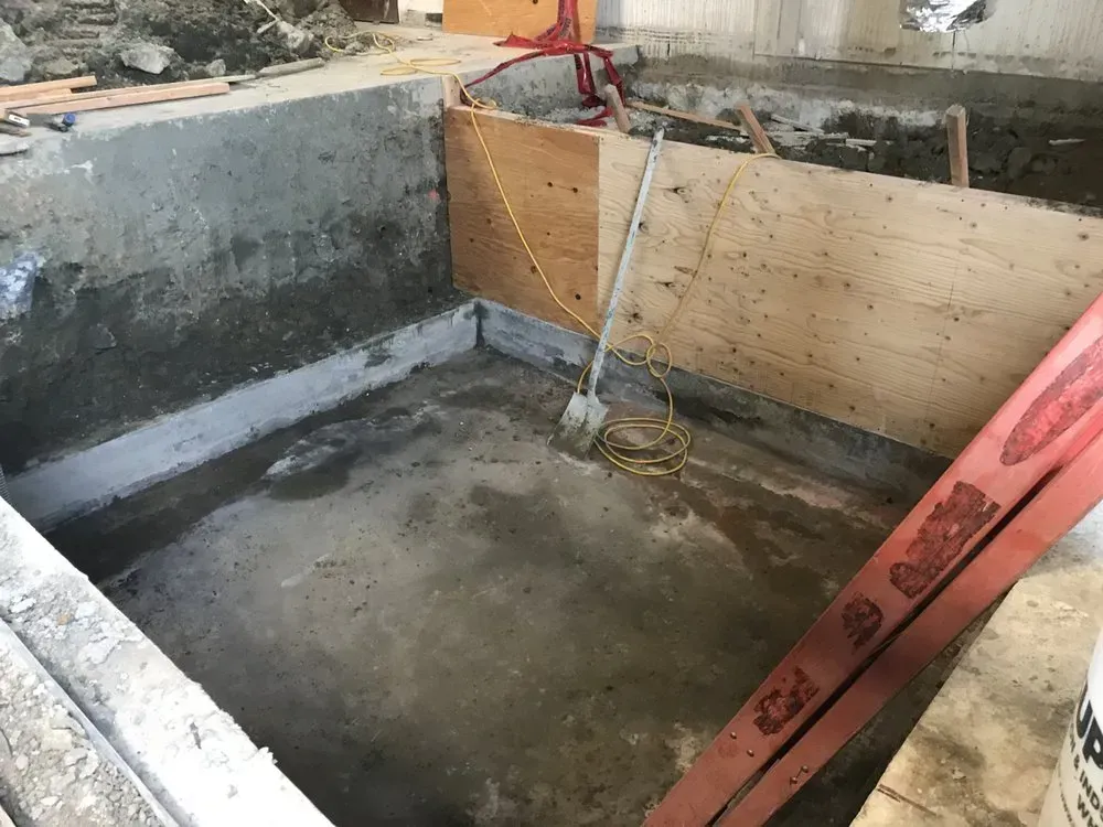 Construction site, cement pit. Wooden paneling, tools, and red ladder.
