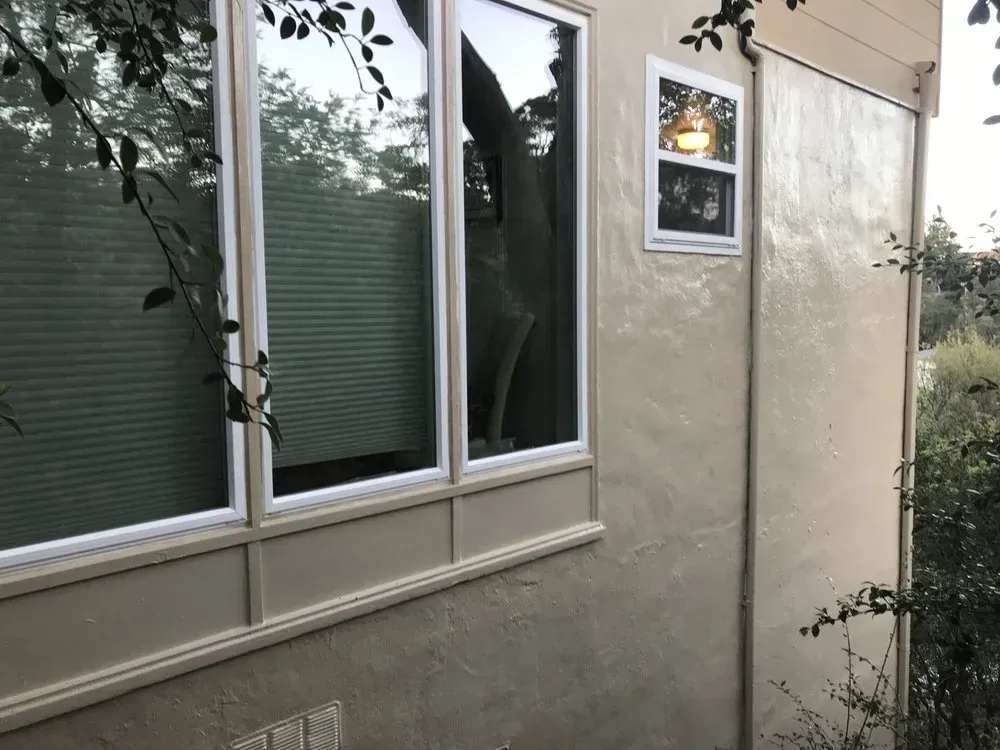 Exterior view of a building with windows. Beige stucco wall, tree reflected in large window, smaller window above.