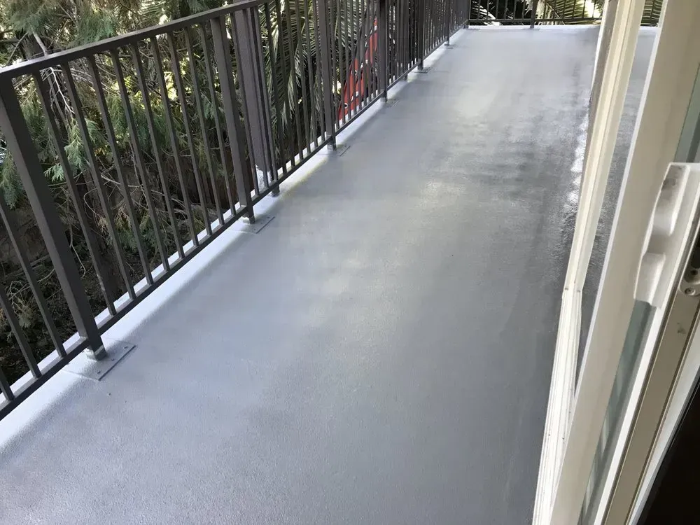 A gray, newly coated balcony with a metal railing and sliding glass door, surrounded by trees.
