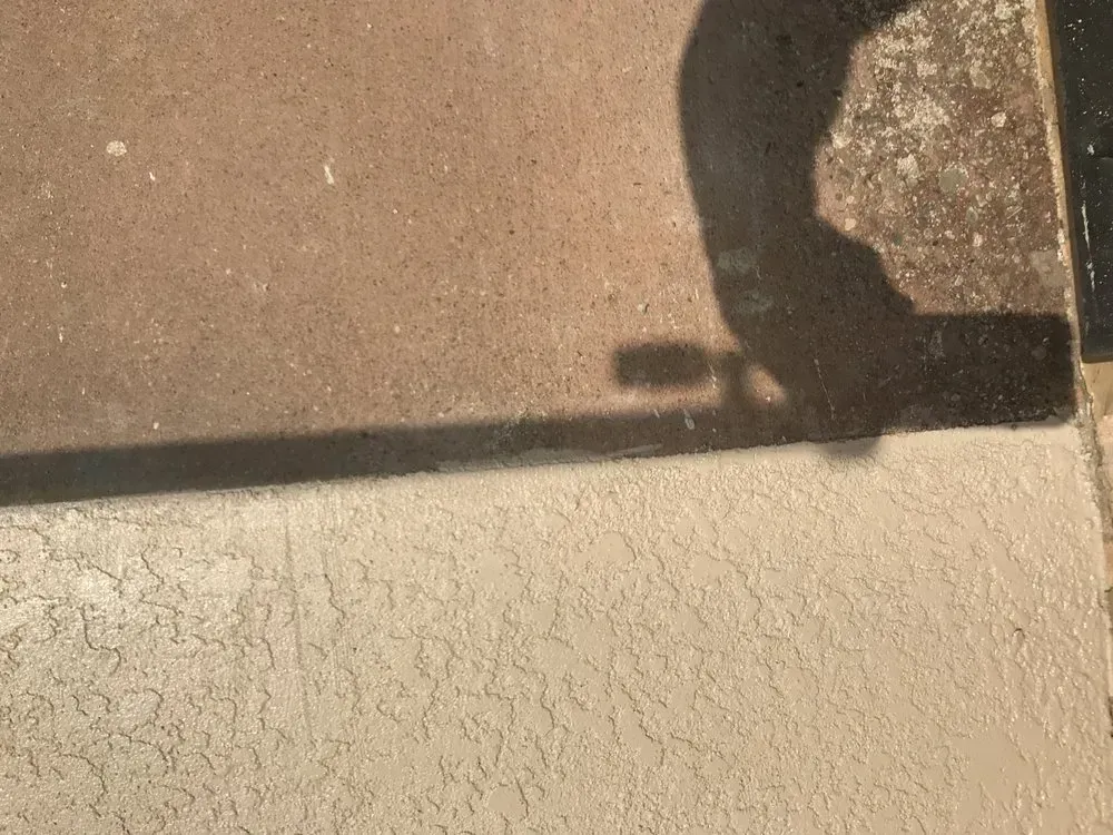 Shadow of a person on tan-colored concrete, with a contrasting lighter-toned stucco surface in the foreground.